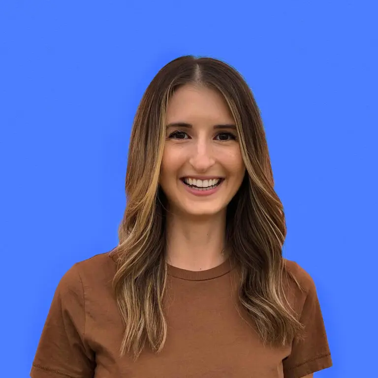 Smiling woman with long brown hair wearing a brown shirt against a blue background.
