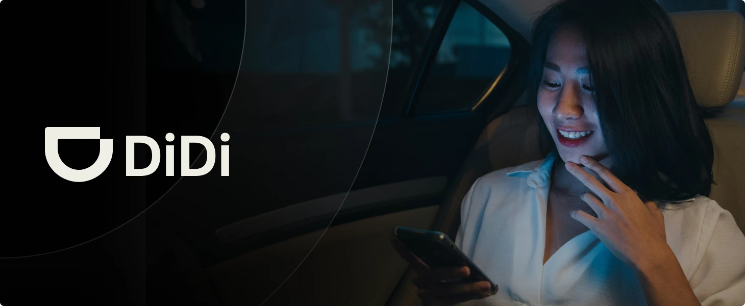 Smiling woman using smartphone inside a car at night with DiDi logo on the left side.