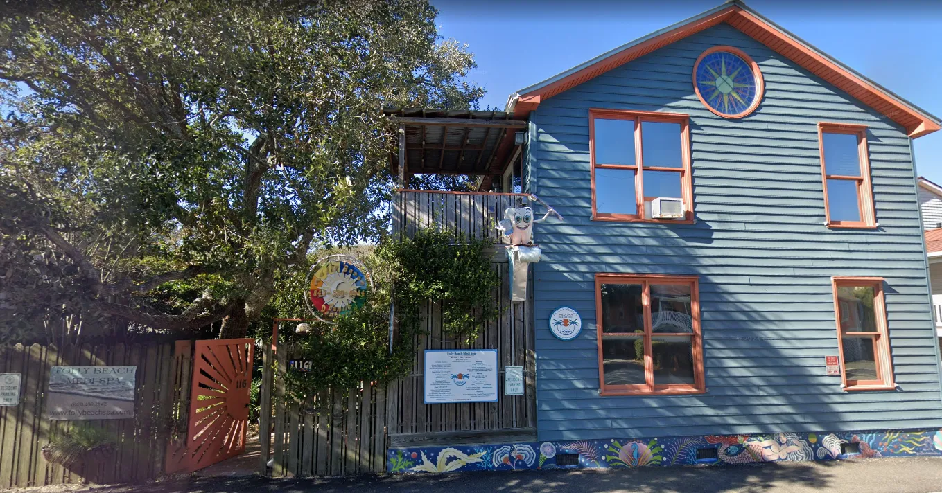 Blue exterior building with coral trim, a sun-themed gate, a colorful mural along the base, and signs indicating Folly Beach Medi Spa.