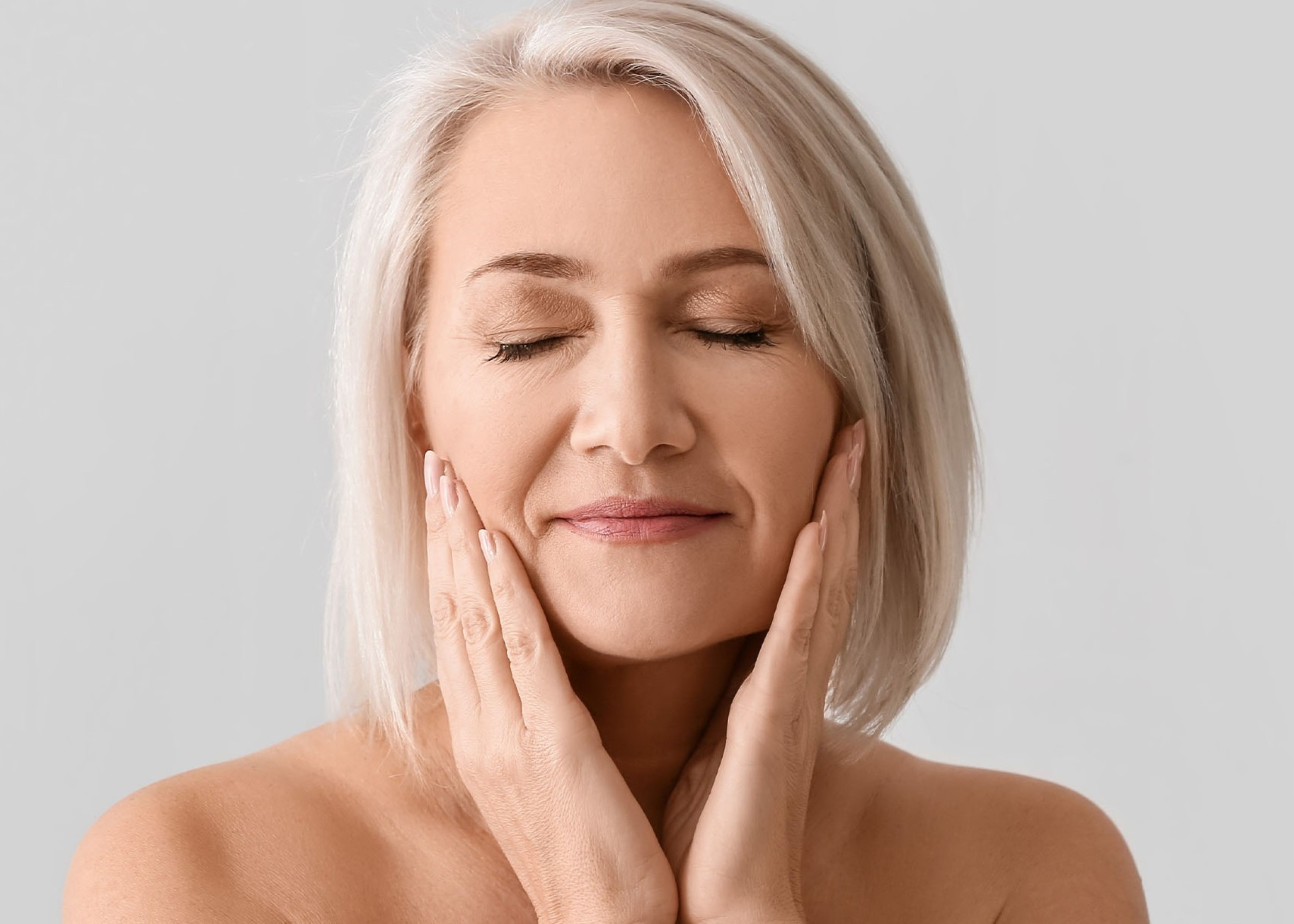 Content middle-aged woman with closed eyes gently touching her face with both hands.
