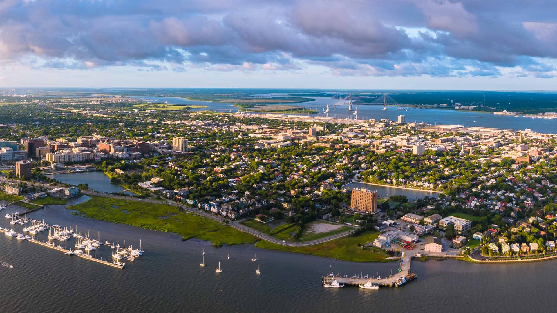 Aerial view of an island town with the ocean in the distance and a marina in the foreground. The island is a mix of homes and green.