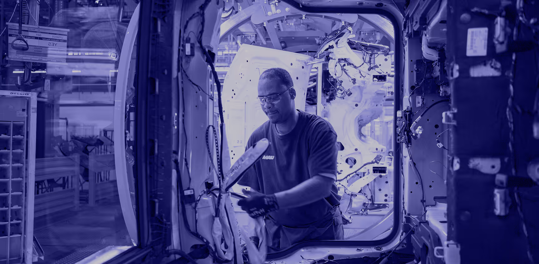 MAU-branded worker in safety glasses performing assembly work inside an automotive vehicle — skilled industrial staffing in action