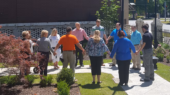 MAU employees gathered in a circle holding hands outdoors — reflecting the company's faith-based values