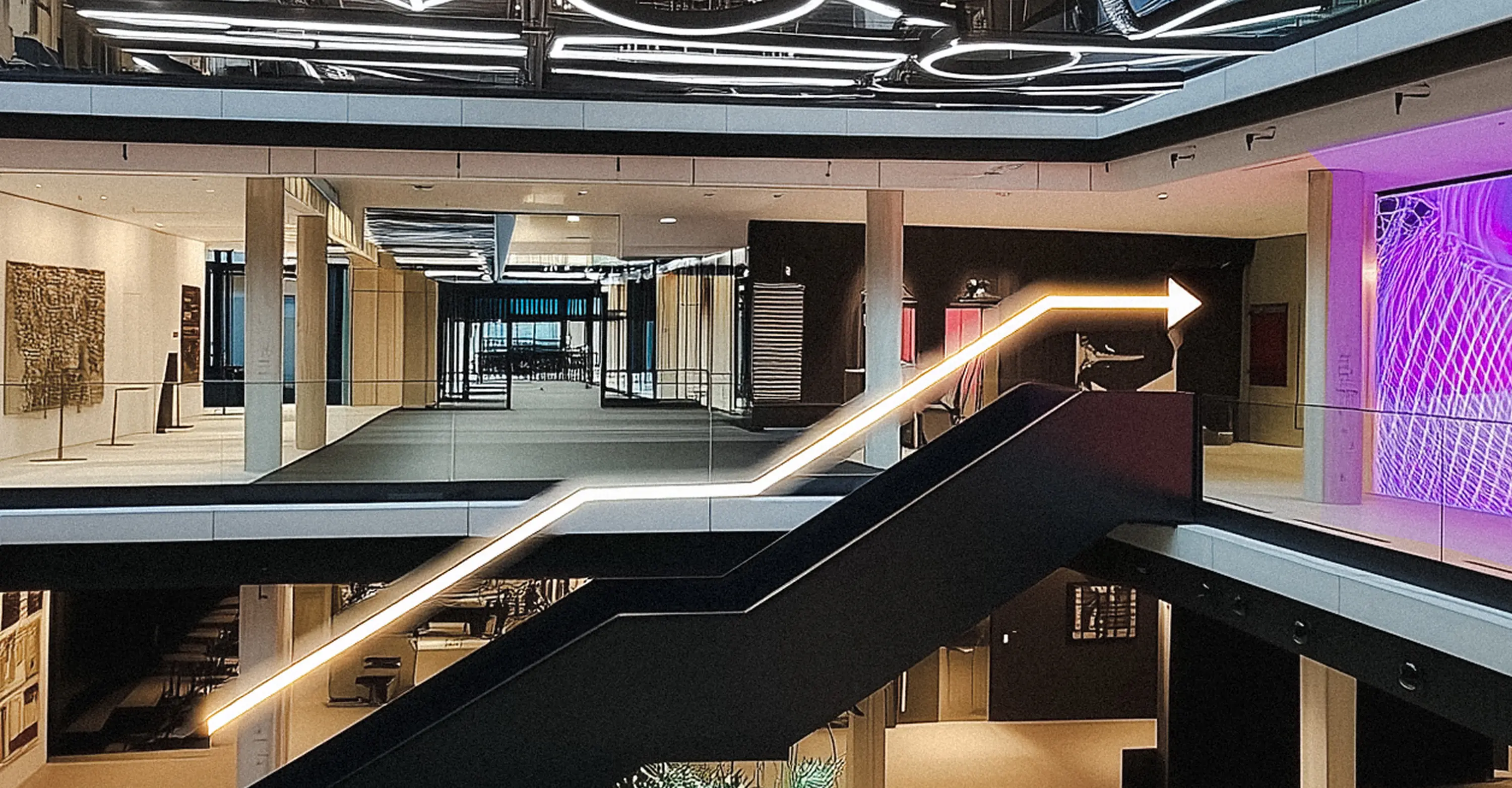 Modern interior with a black staircase featuring a lighted handrail shaped like an arrow pointing upward and to the right.