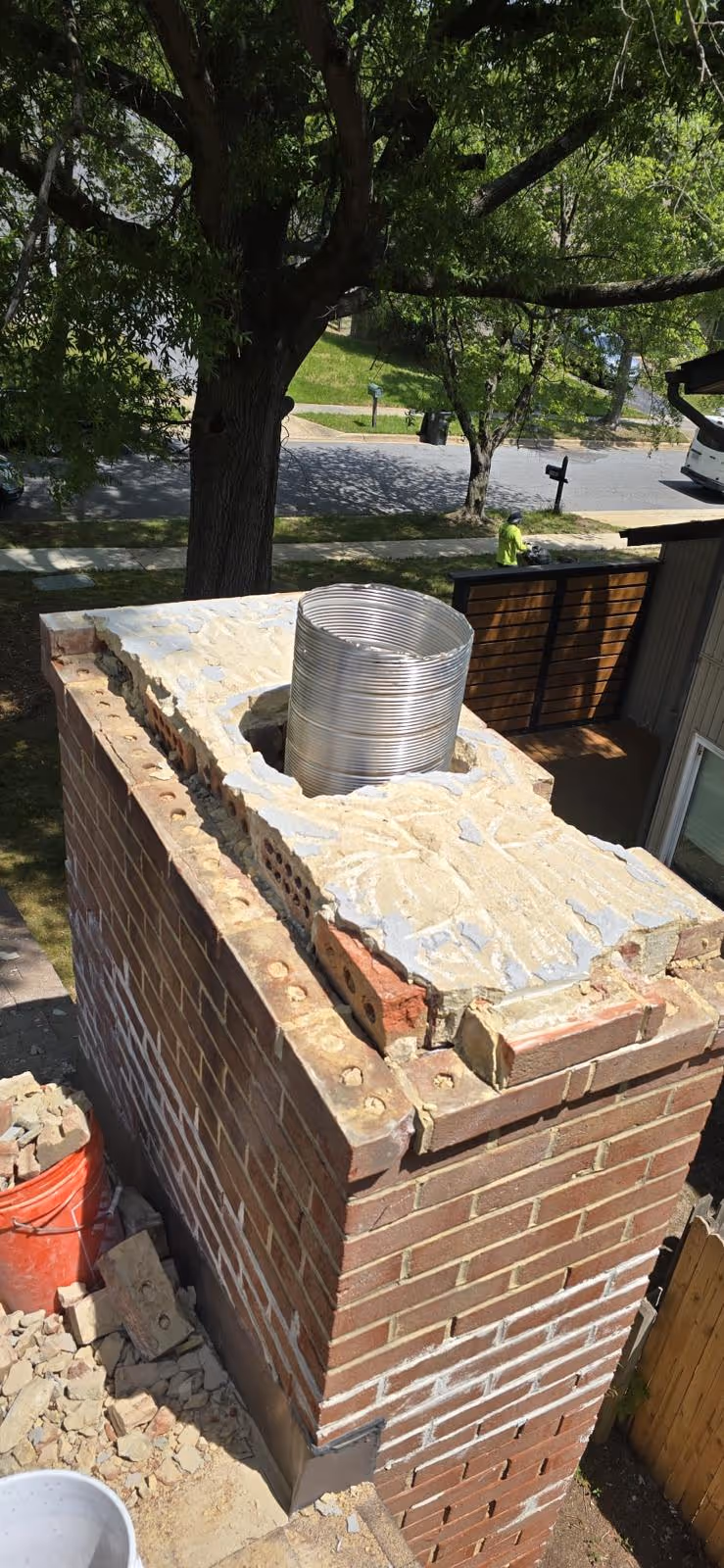 Partially dismantled brick chimney with a metal flue pipe inside, surrounded by construction debris and tools.