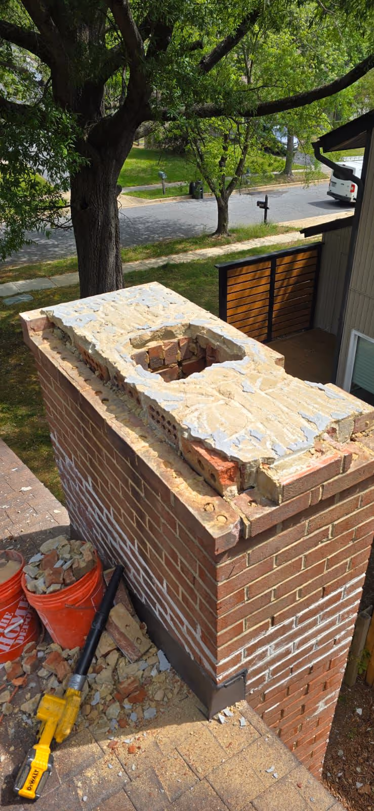 Partially demolished red brick chimney on a roof with debris and a yellow DeWalt power tool nearby.