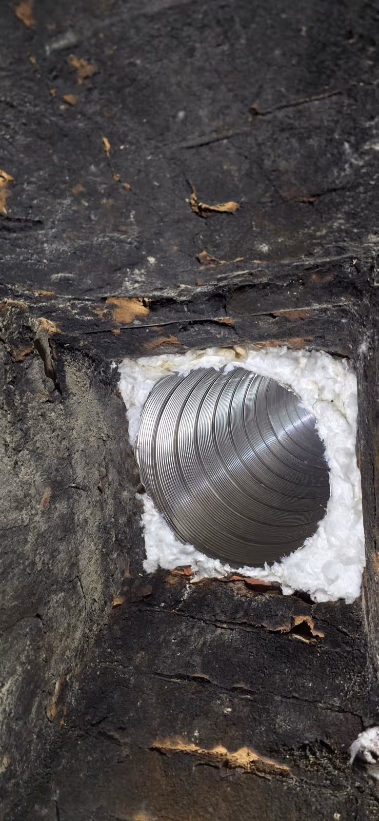 Close-up of a metal duct vent installed in a wall cavity insulated with white foam.