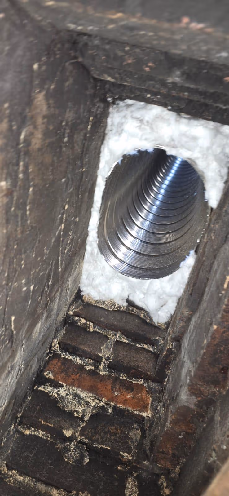 Close-up view of a metal ventilation or duct pipe inside a brick chimney with white insulation around the pipe opening.