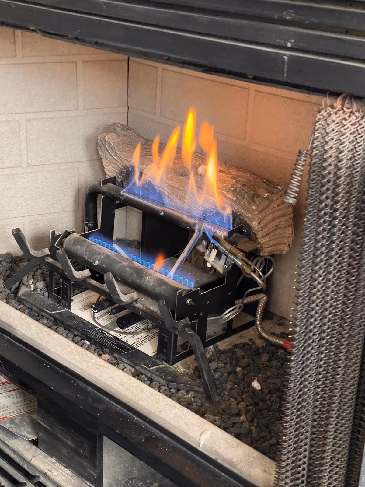 Gas fireplace burner with blue and yellow flames and a ceramic log inside a stove.