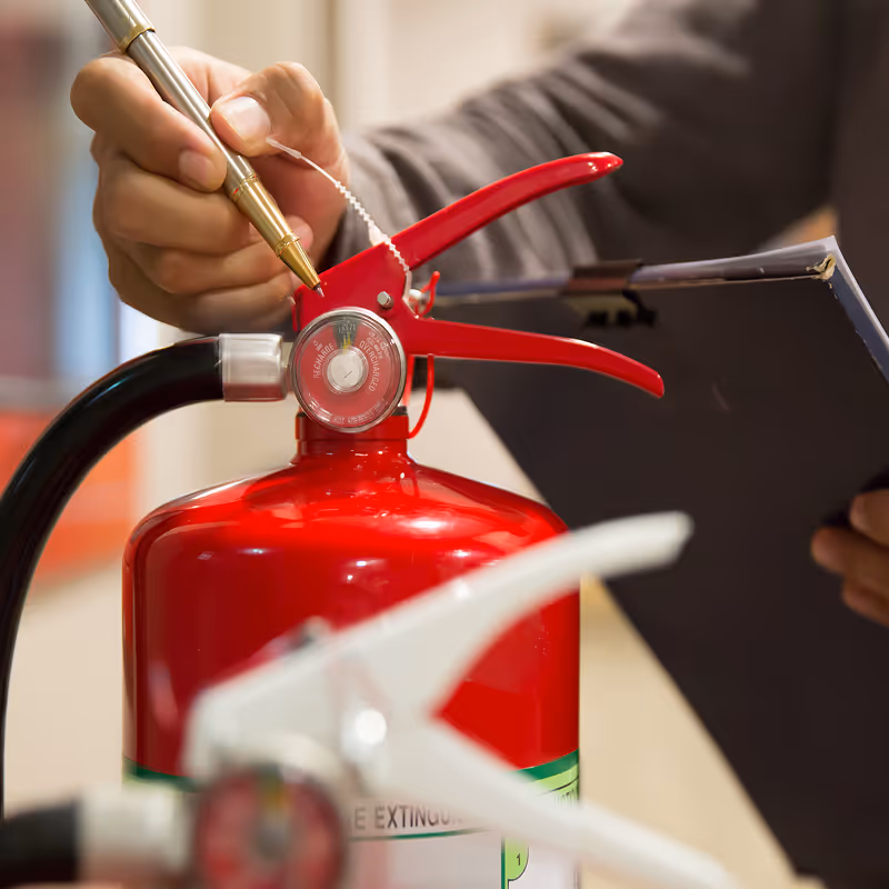 Person inspecting a red fire extinguisher with a pen and a clipboard in hand.