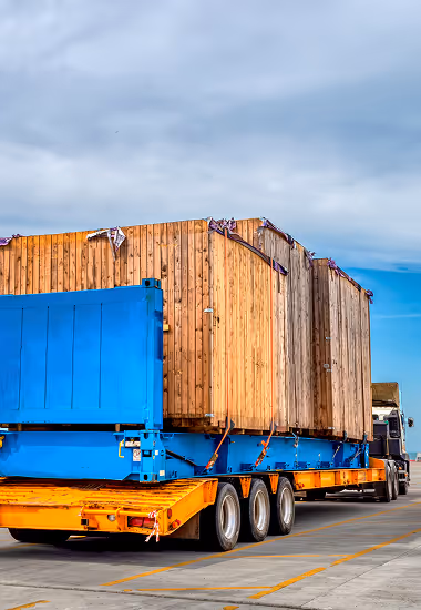 Flatbed truck transporting large wooden crates secured with straps under a partly cloudy sky.