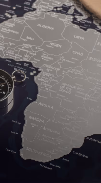 Close-up of a black and gray map focusing on Africa with a silver compass on the left side.