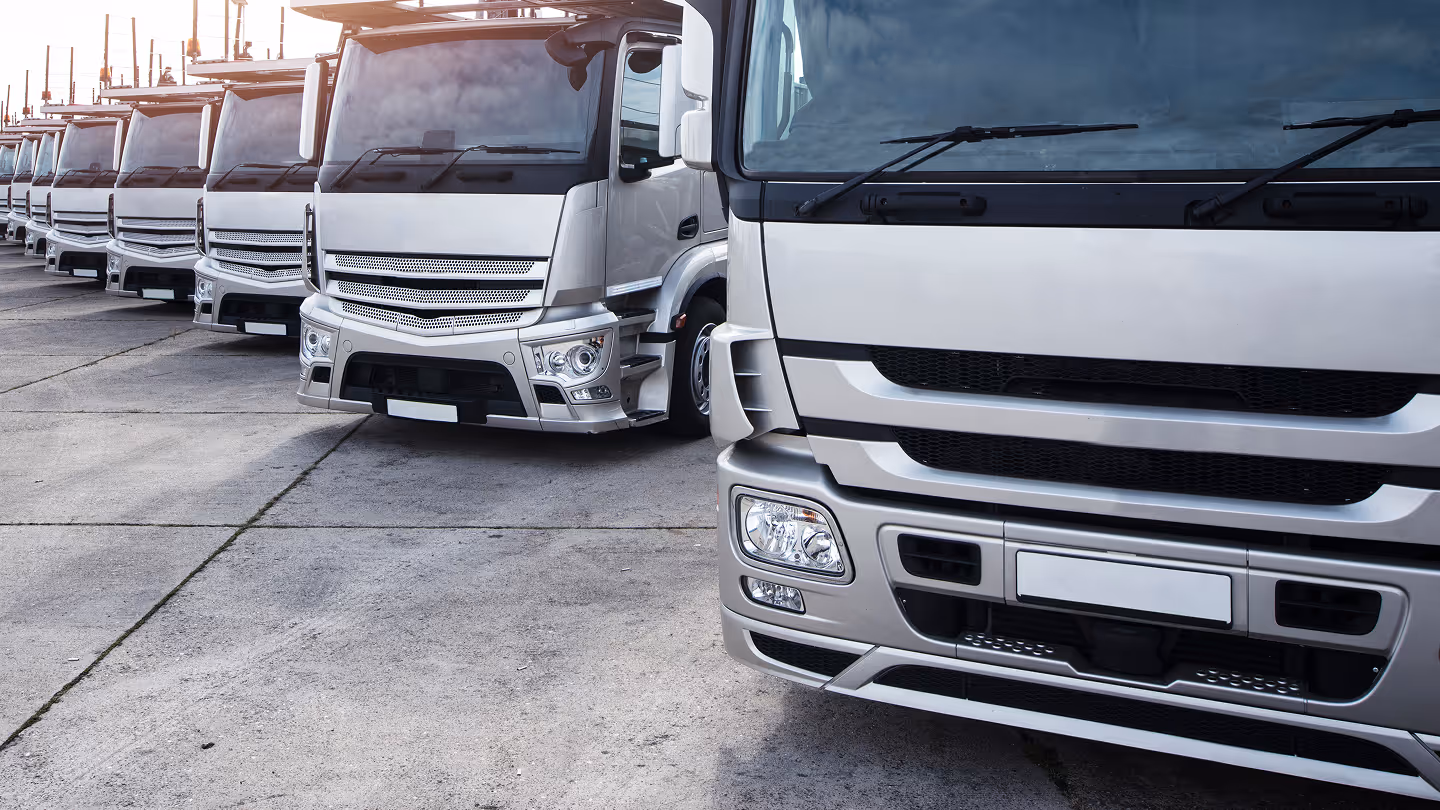 Row of white semi-trucks neatly parked on a concrete lot, seen from the front right side.