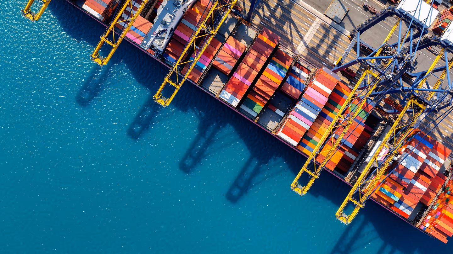 Aerial view of a dock with colorful shipping containers and yellow cranes extending over blue water.