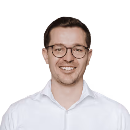 Lächelnder Mann mit Brille und weißem Hemd vor weißem Hintergrund.