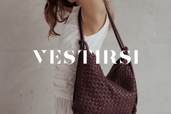 Woman in a white dress holding a large dark brown woven leather handbag on her shoulder with a neutral background and the text VESTIRSI.