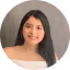 Smiling young woman with long dark hair wearing a black top against a neutral background.