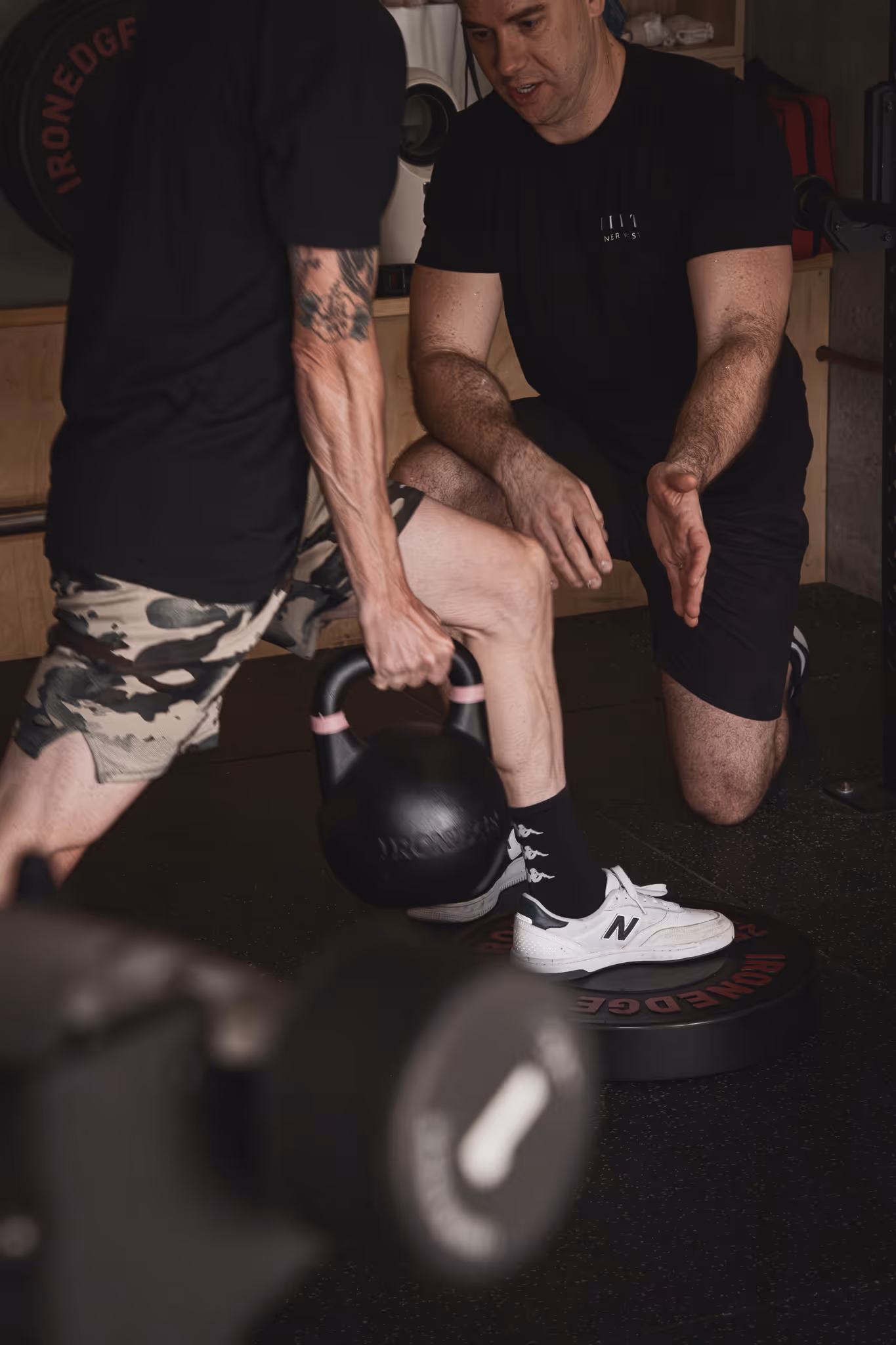 Trainer guiding a man holding a kettlebell during a workout in a gym setting.