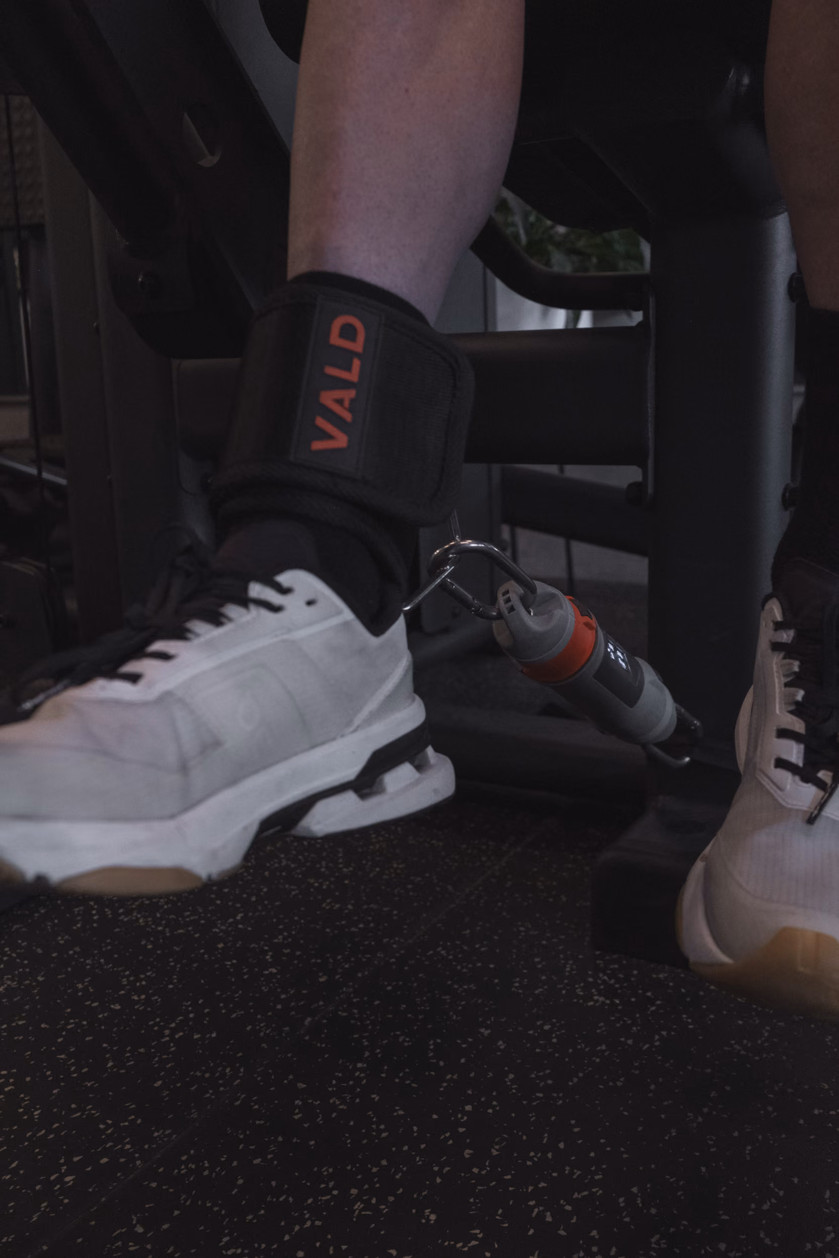 Person wearing a VALD ankle strap attached to gym equipment for leg exercise.