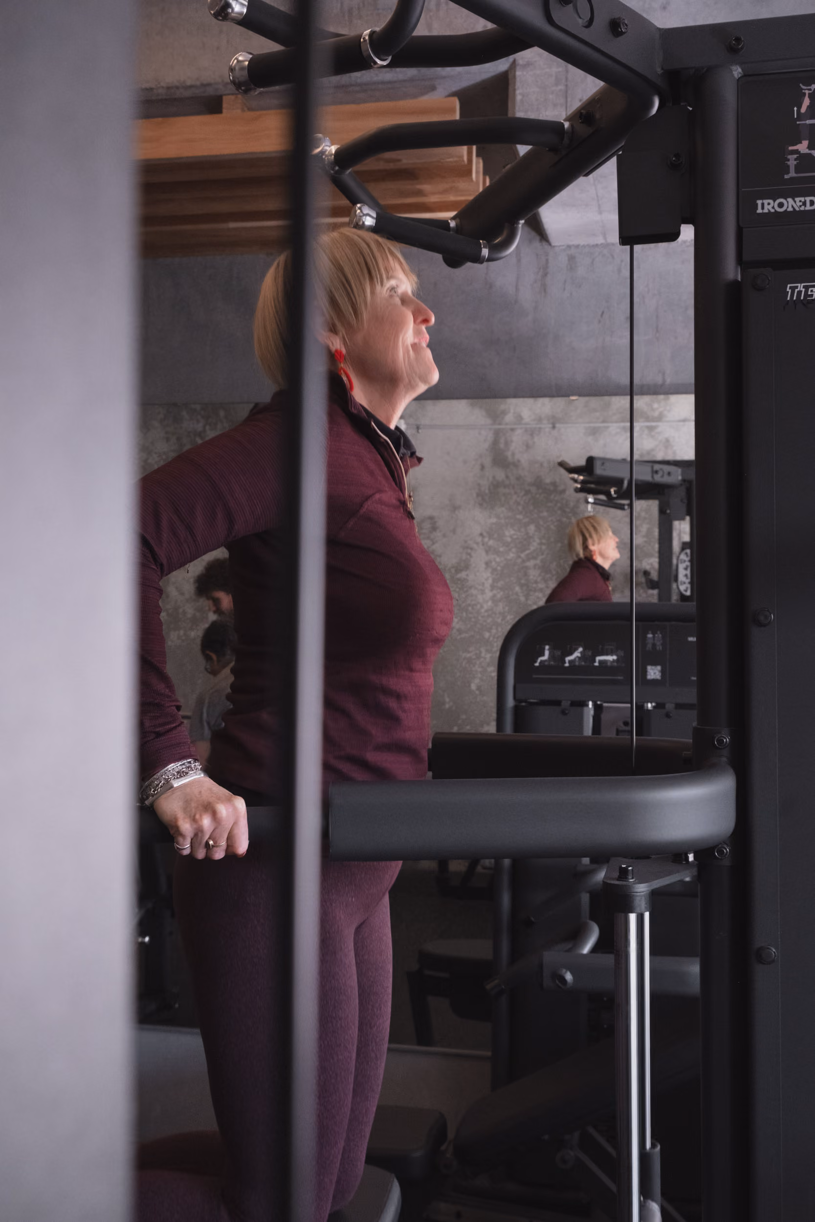 Woman in maroon workout clothes using gym equipment to perform tricep dips indoors.
