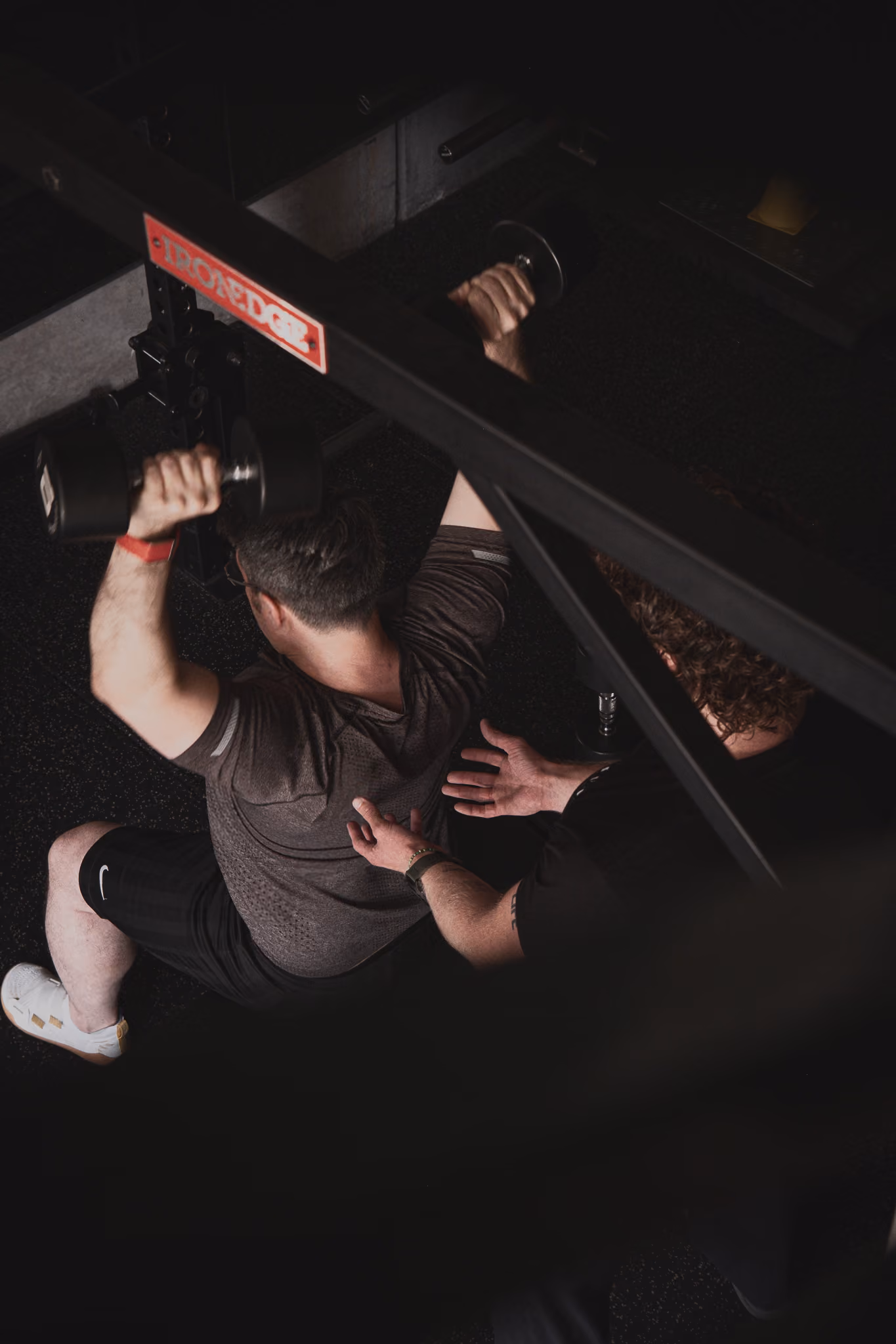 Overhead view of a man lifting dumbbells while another spotter assists in a gym setting.