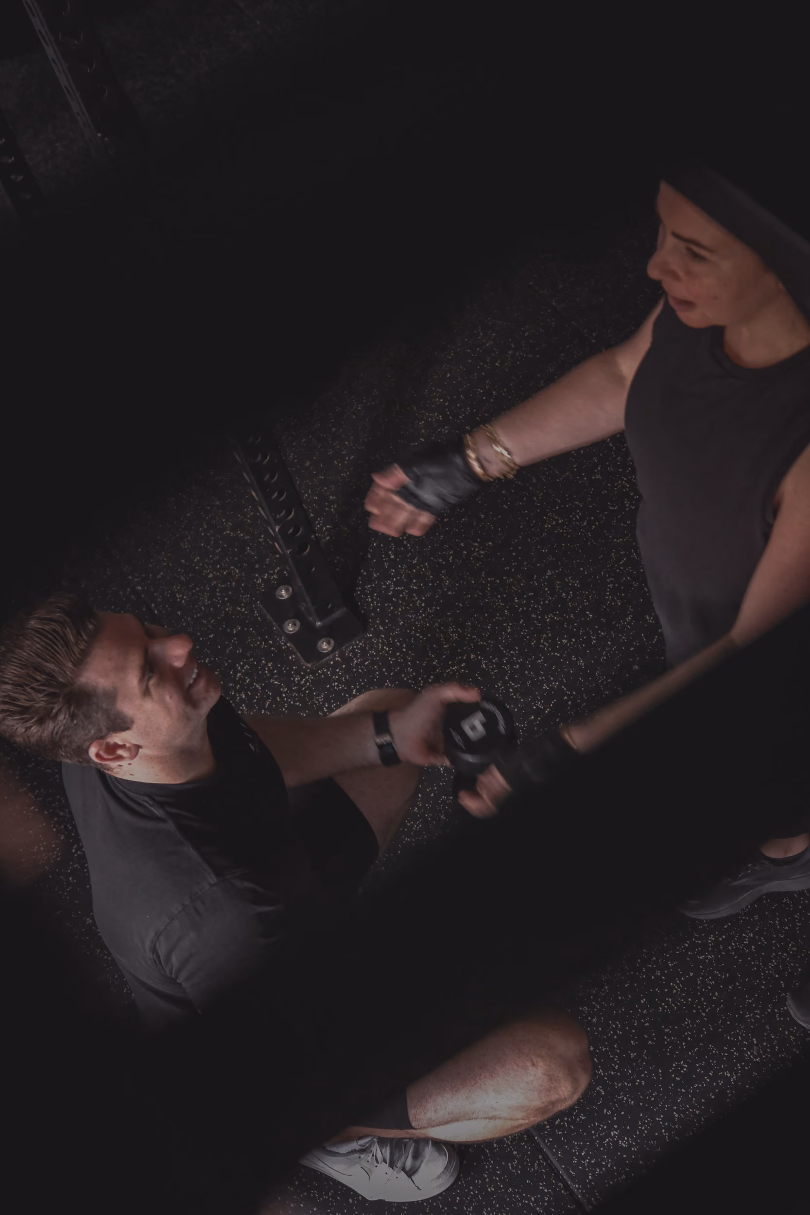 Two people at gym, one seated holding dumbbell, the other standing offering support.