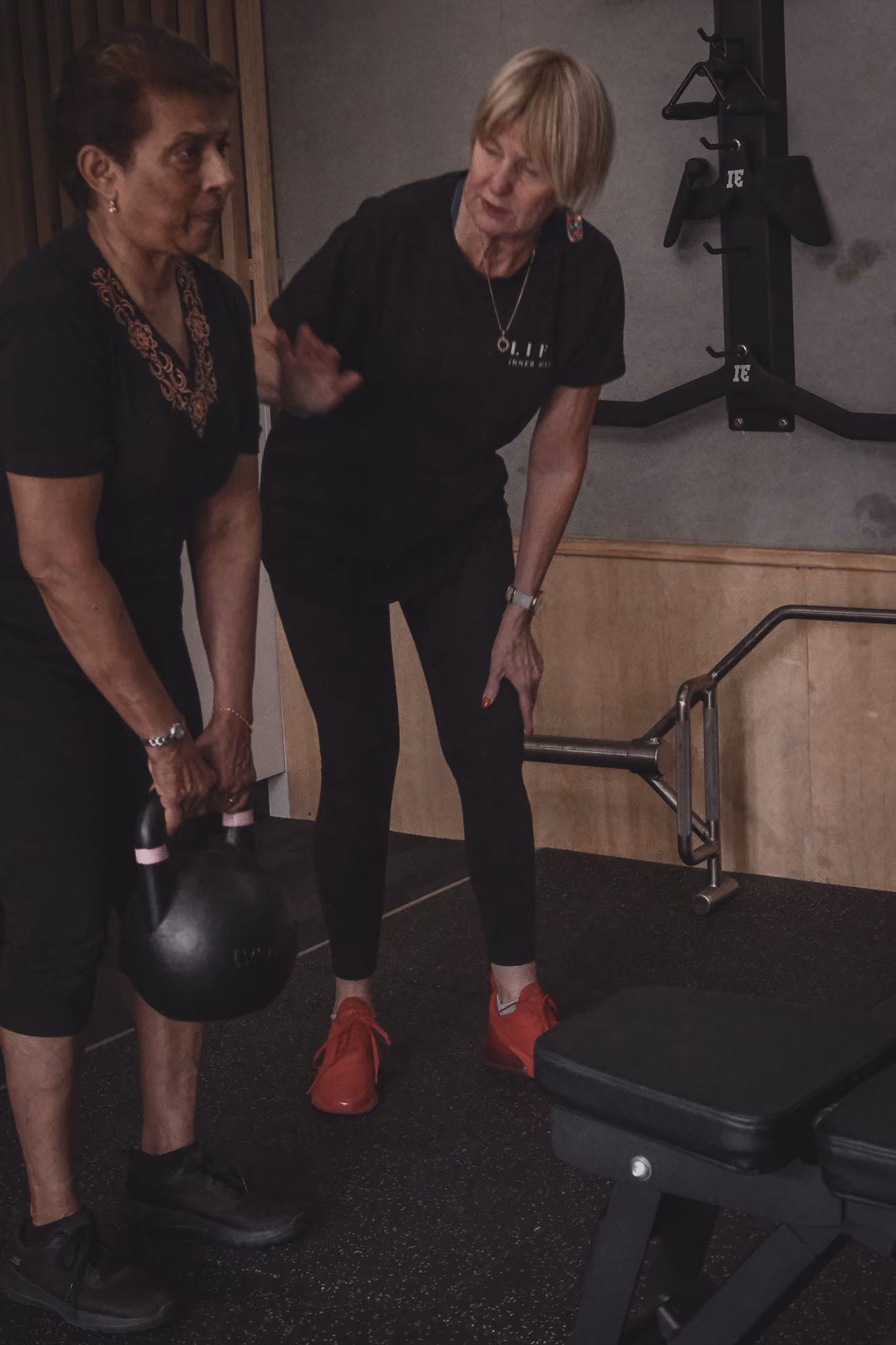 Woman coaching another woman lifting a kettlebell in a gym setting.