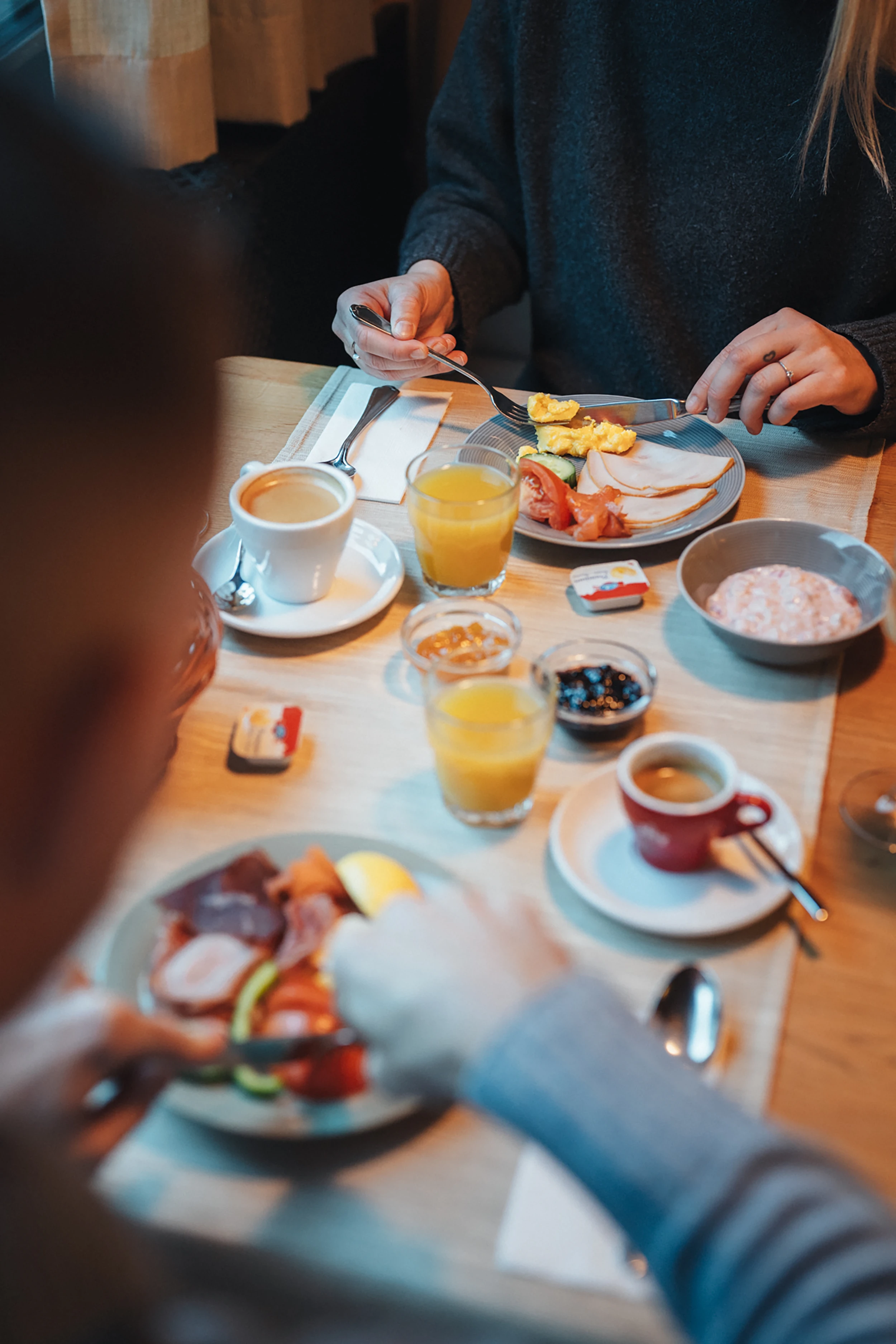 Gäste geniessen ein reichhaltiges Frühstück im Alpen Resort Zermatt mit Rührei, Aufschnitt, frischem Orangensaft, Kaffee und Birchermüesli an einem gemütlich gedeckten Holztisch.