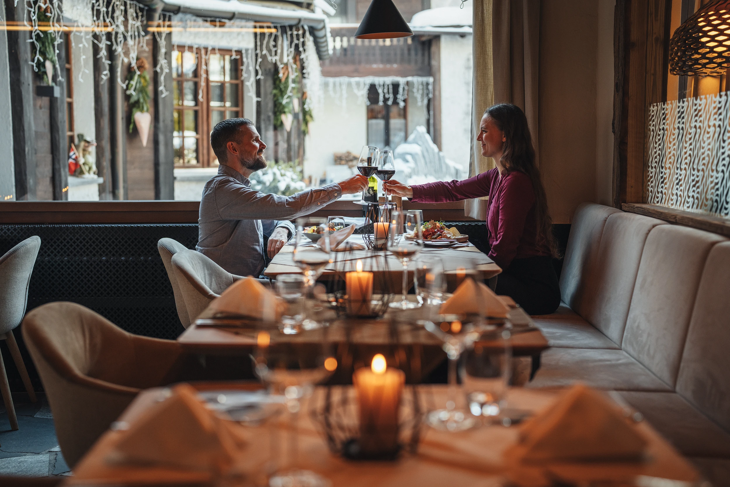 Ein Paar stösst in der gemütlichen und eleganten Atmosphäre des Restaurants PeakFine mit Rotwein an, während sie ein feines Abendessen bei Kerzenschein an einem festlich gedeckten Tisch geniessen.