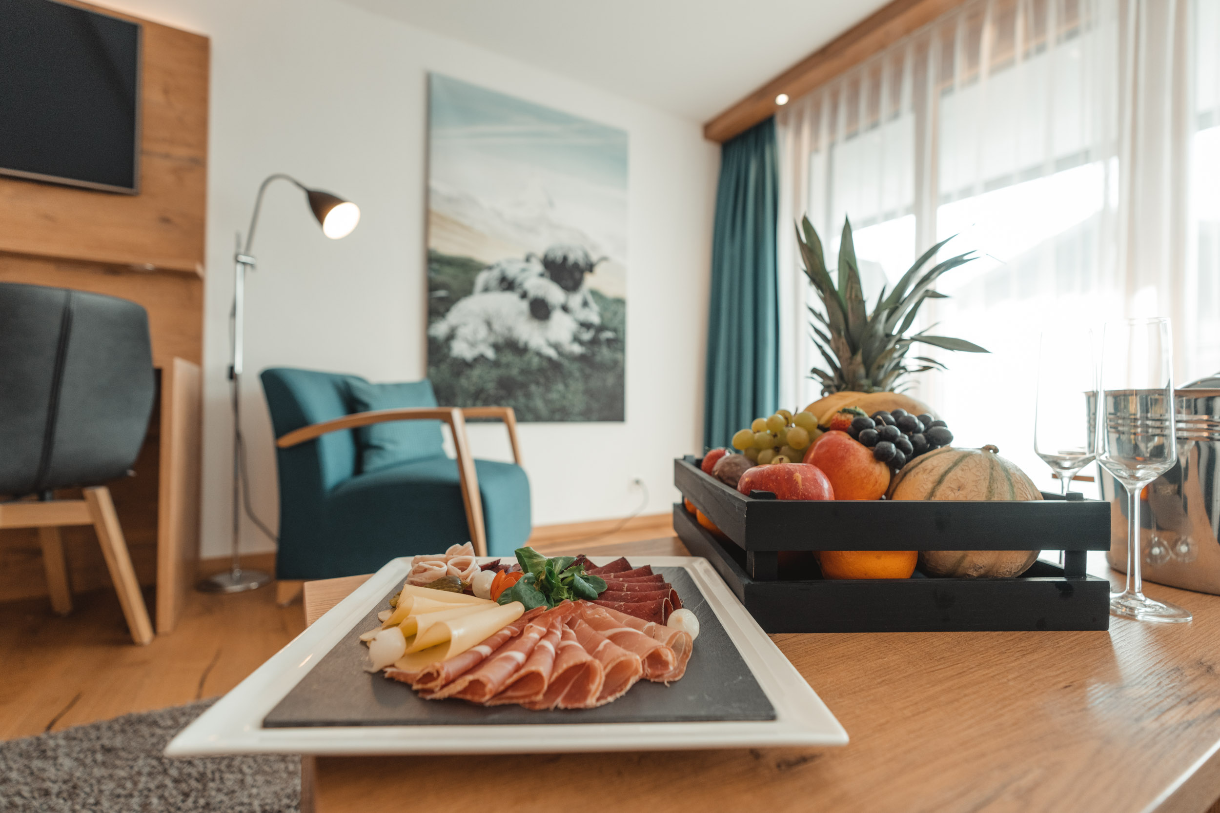 Ein herzlicher Empfang im Hotelzimmer des Alpen Resorts Zermatt mit einer Walliser Trockenfleisch- und Käseplatte auf Schiefer sowie einem Korb mit frischen Früchten auf einem hellen Holztisch.