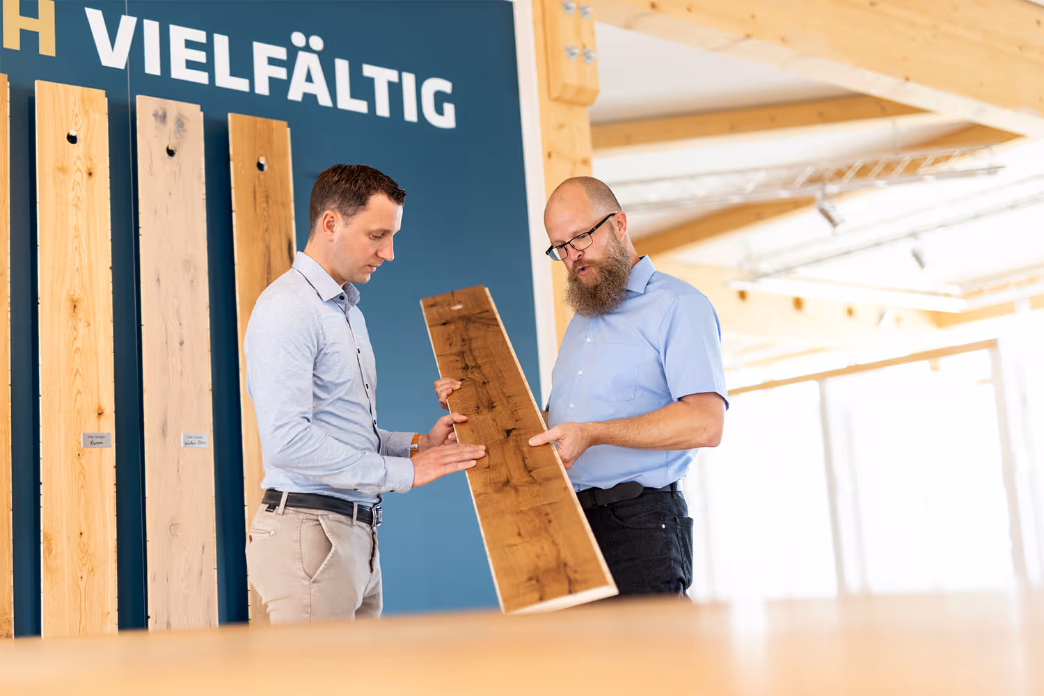Ein Berater und ein Kunde sind auf dem Bild zu sehen, wie sie ein Stück Parkett betrachten.