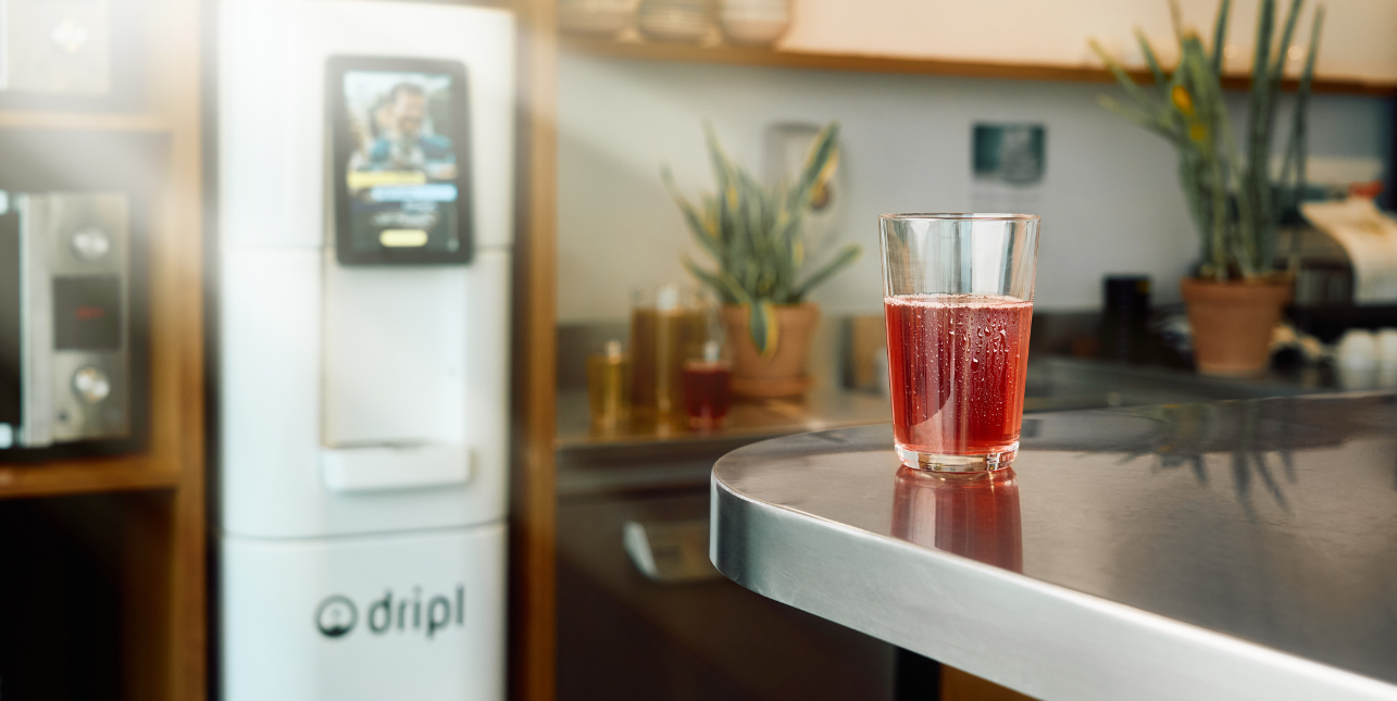 Een Dripl refill point, de slimste waterdispenser, en een glas gevuld met water met een gezond smaakje. 