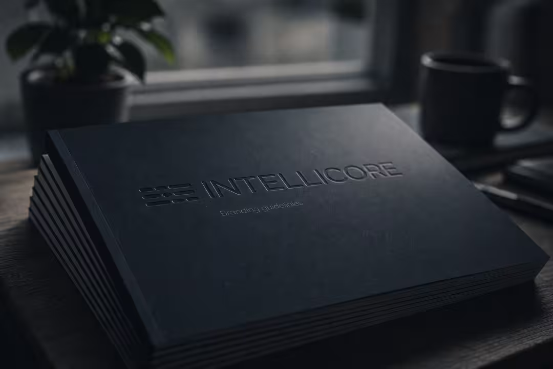 Black embossed Intellicore branding guidelines book on a wooden desk.