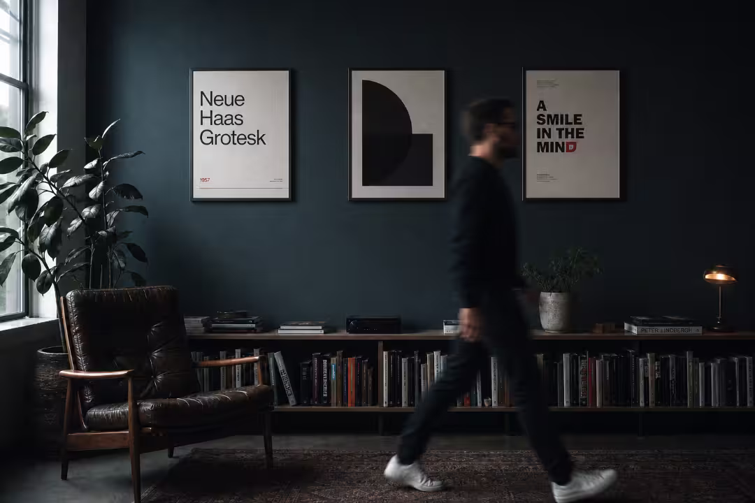 Dark blue studio wall featuring framed design posters, a leather armchair, and a bookshelf.