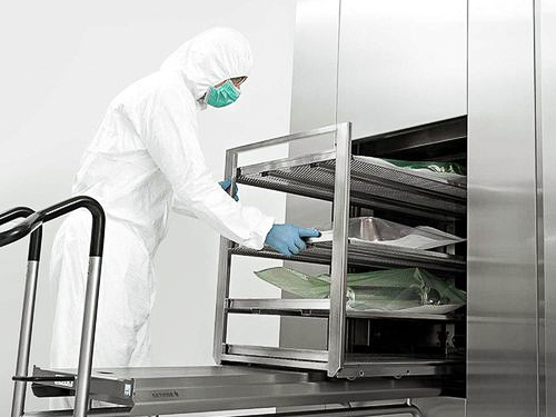 Aseptic isolator with white gloves attached, used for sterile pharmaceutical filling, with a reflection of a person working on a computer behind the glass.
