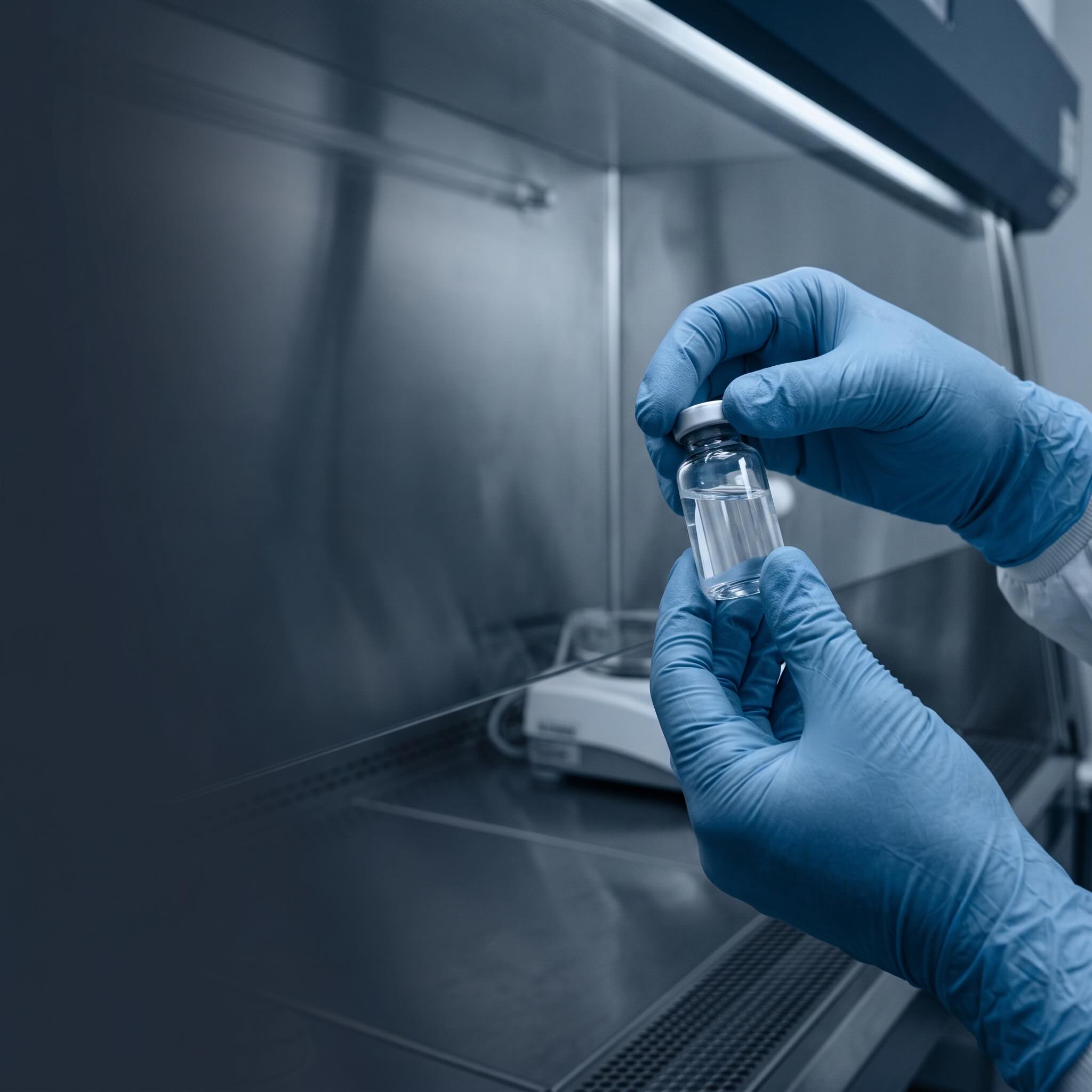 Gloved hands holding a clear biologic vial in a pharmaceutical cleanroom