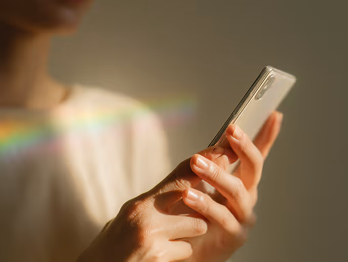 Person holding and interacting with a smartphone in soft natural light with rainbow reflections.