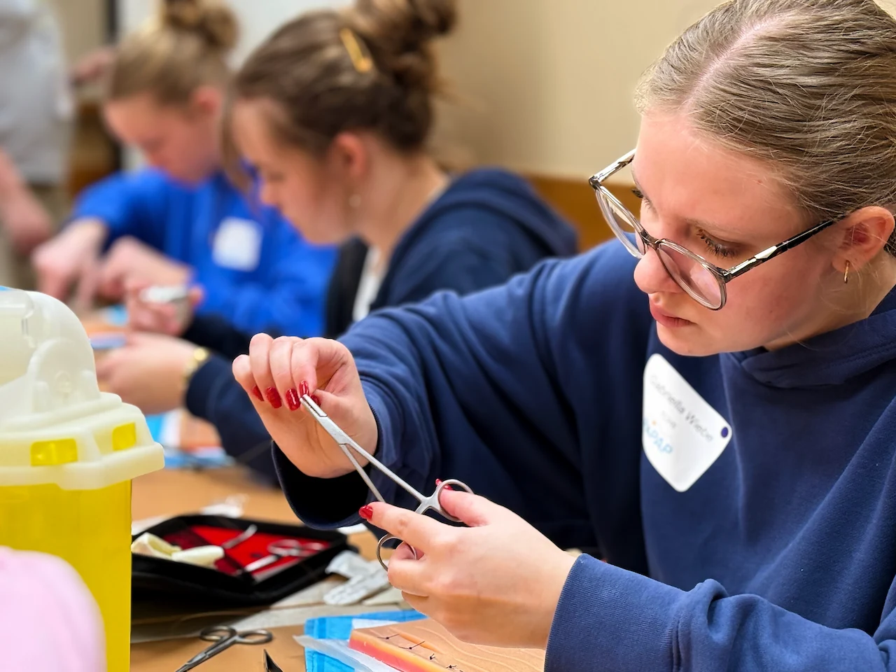 Young woman focused on suturing practice using forceps and needle on a training pad.
