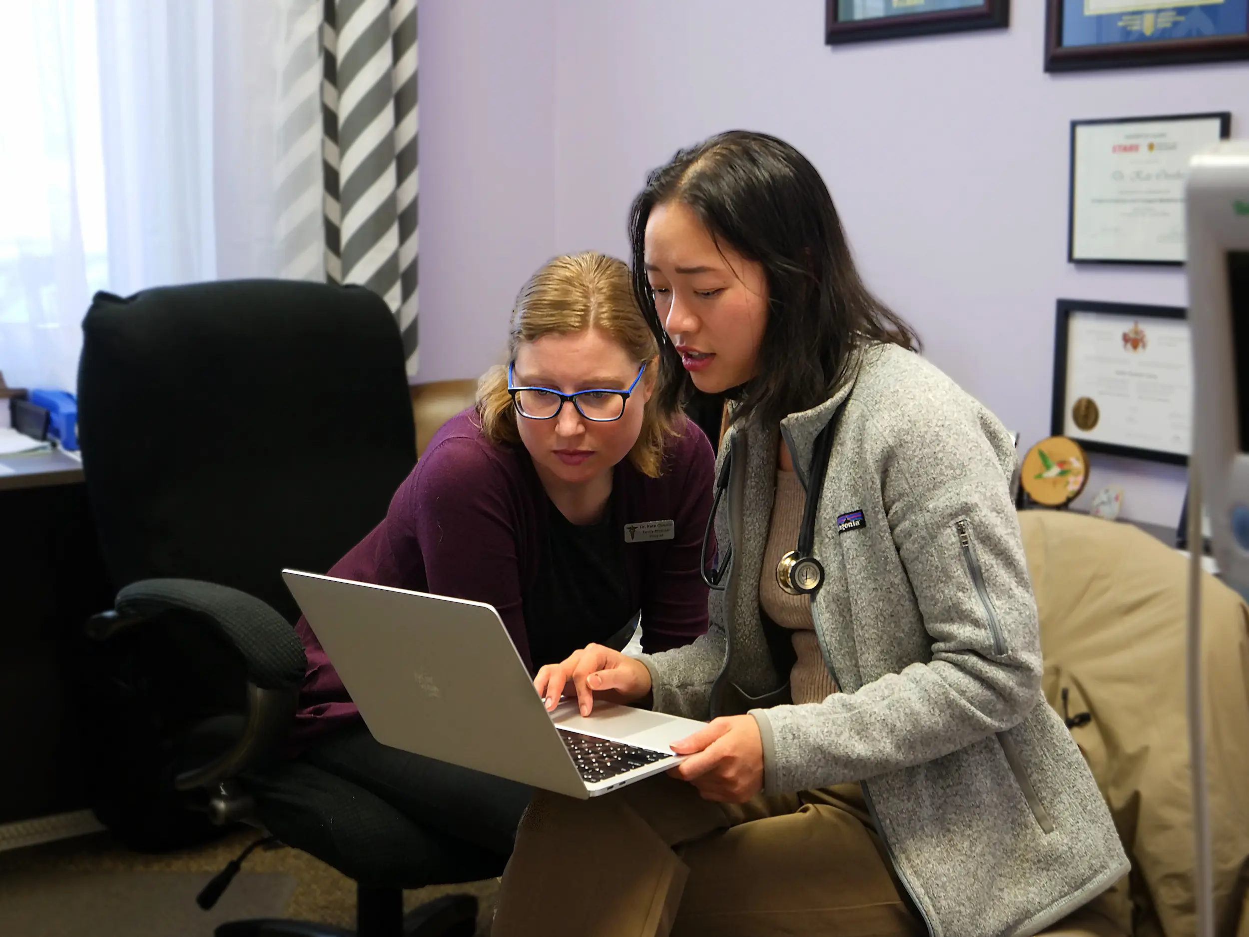 Two medical professionals reviewing information on a laptop in an office with diplomas on the wall.