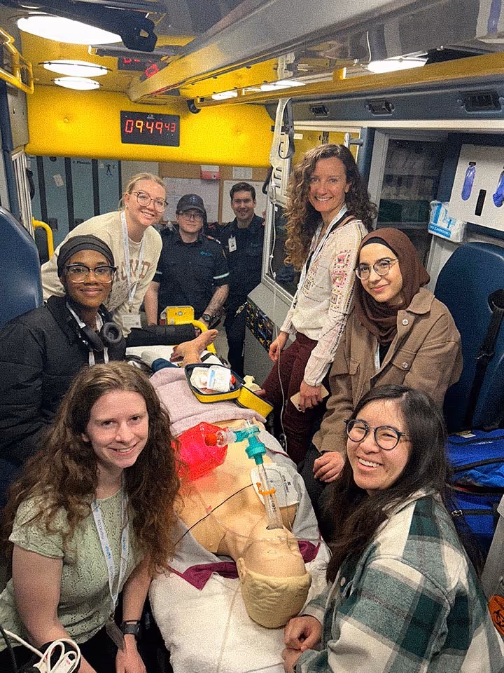 Group of people smiling inside ambulance around a medical training dummy on a stretcher.
