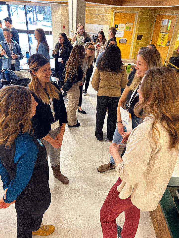 Group of people wearing name tags chatting in a hallway during a social or networking event.