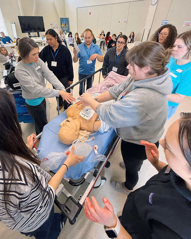 Group of people practicing CPR on a medical training mannequin in a classroom setting.