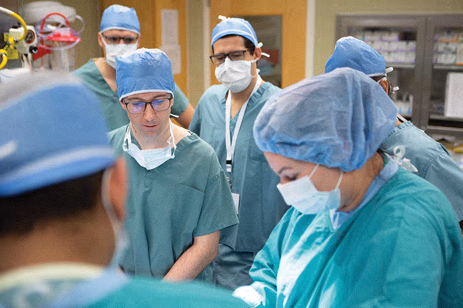Surgeons in green scrubs and masks focused during a surgical procedure in an operating room.