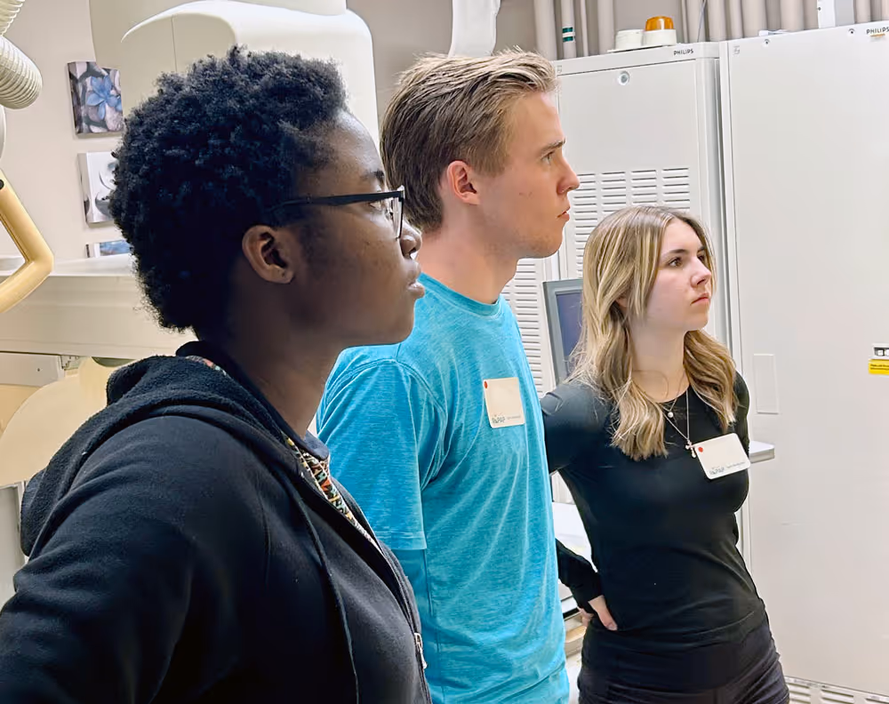 Three young adults attentively listening indoors near white cabinets and electronic equipment.