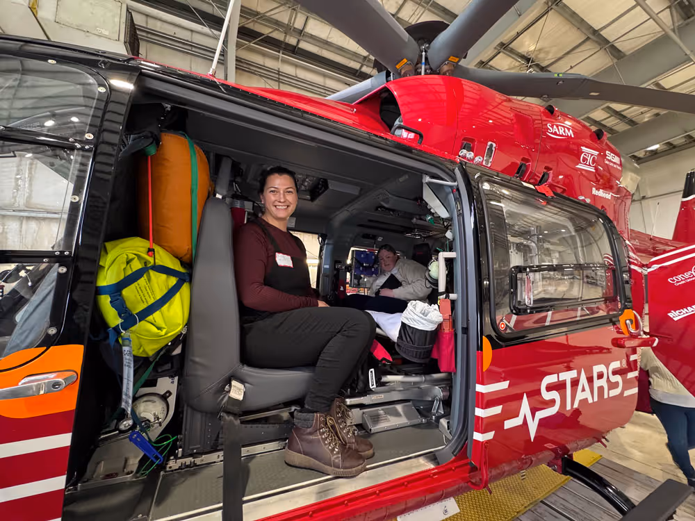 Two women seated inside a red STARS medical helicopter parked in a hangar.