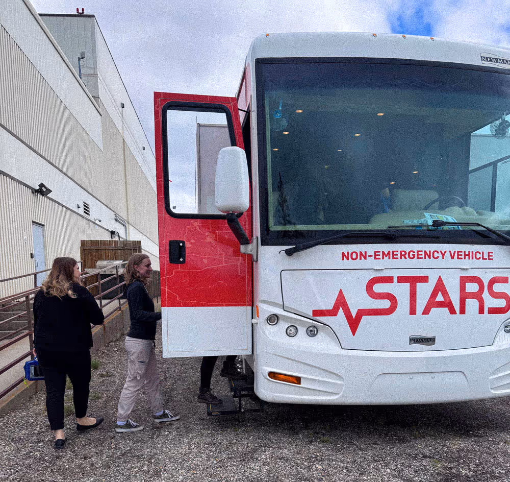 Two women walking toward the open door of a white and red non-emergency STARS vehicle bus.
