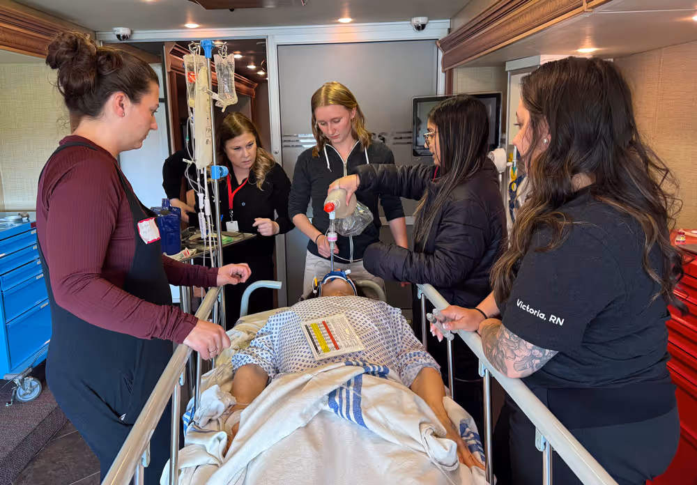 Medical team attending to a patient on a hospital bed inside a clinical room.