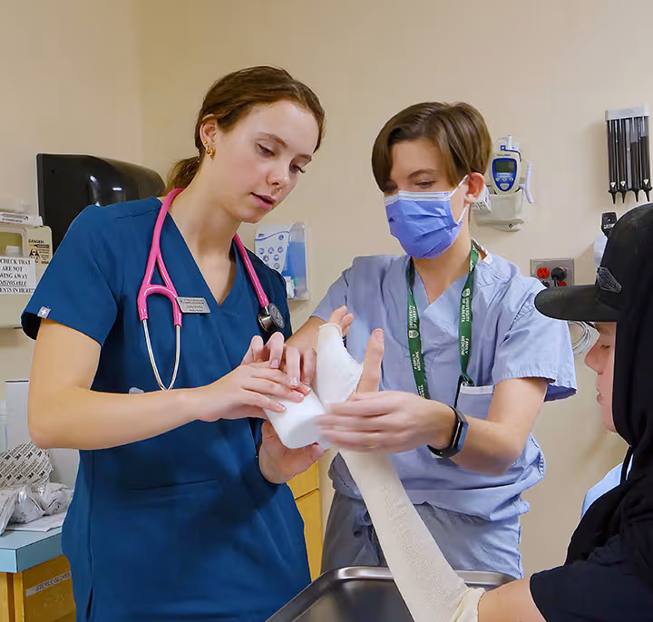 Two healthcare workers applying a bandage to a patient's arm in a clinical setting.