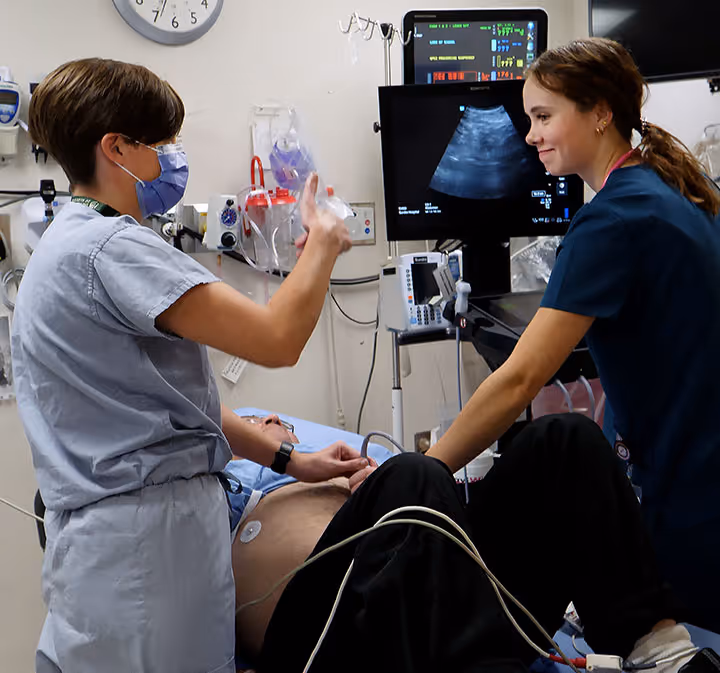 Two healthcare professionals performing an ultrasound on a patient's abdomen in a clinical setting.