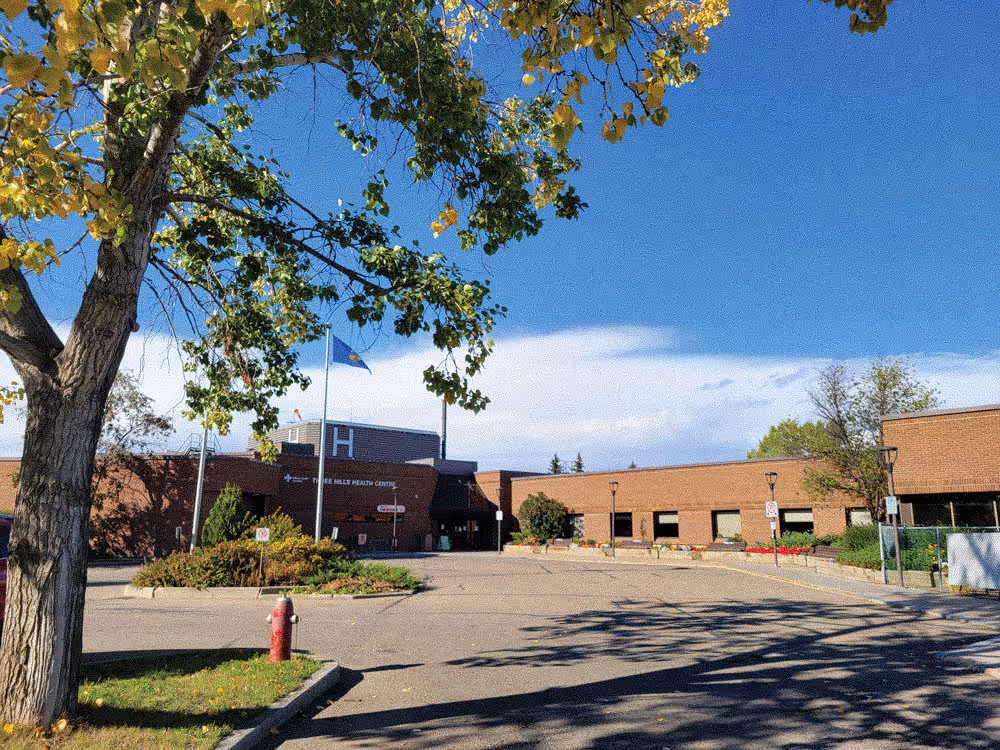 Brick hospital building under blue sky with tree and empty parking lot in front.